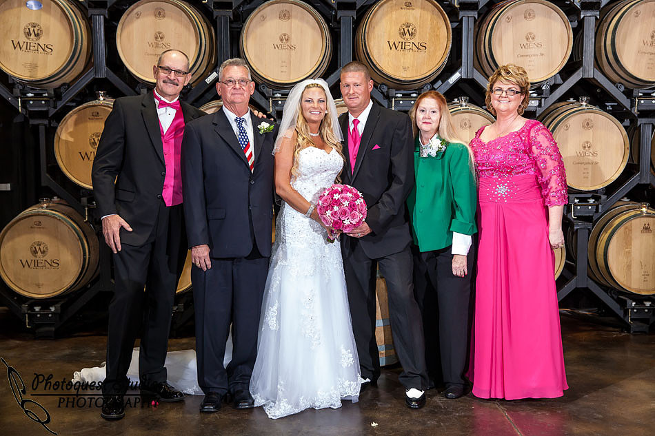 bride and groom and both side parents portrait in the barell room at Wiens family cellars temecula winery by temcula wedding photographer