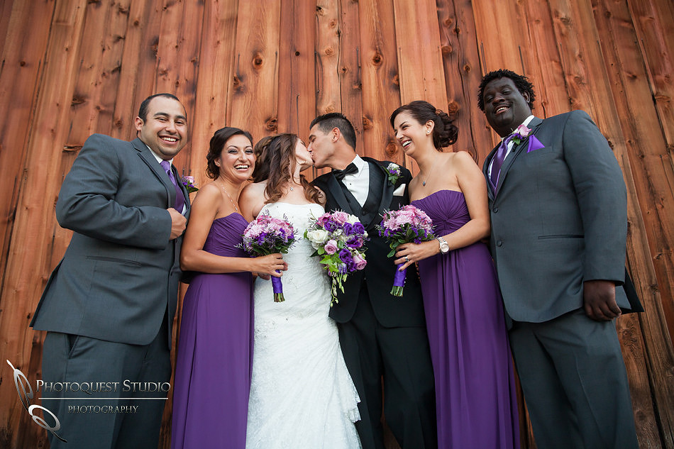 bride and groom kissing and the bridal party cheering at Falkner winery wine wedding by temecula wedding photographer